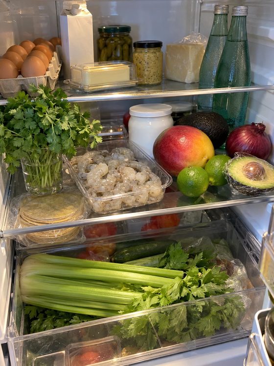 La nevera de Alma abierta, con langostinos, mango, limas, cilantro, yogur griego, aguacate y un manojo de apio